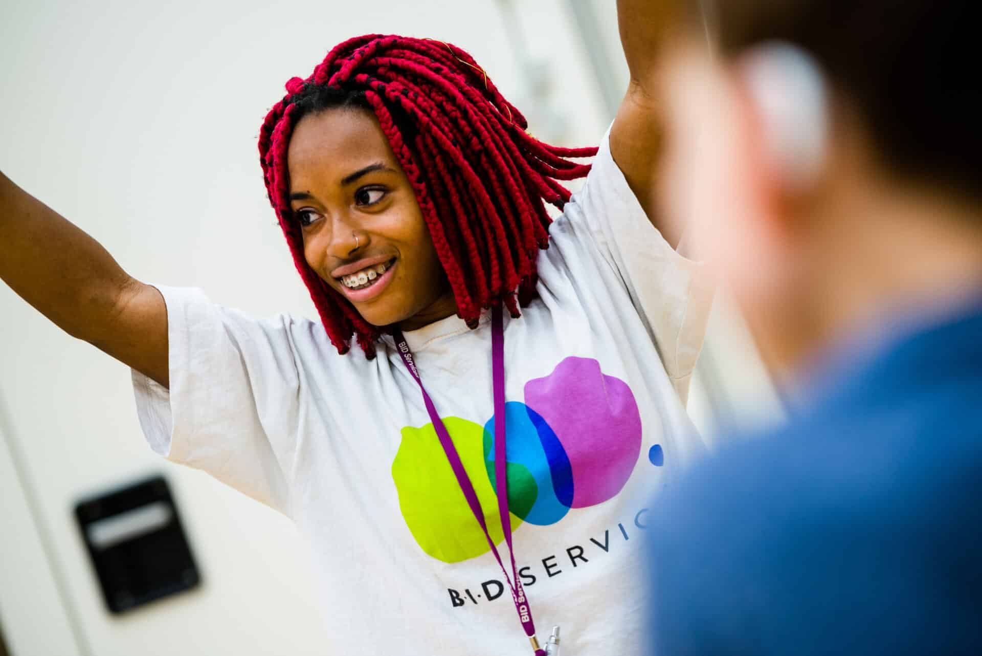 Female wearing BID Services t-shirt with her hands in the air taking part in an activity smiling at someone off screen.