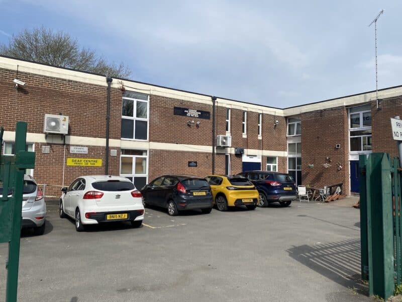 A brown brick building with a sign saying 'Deaf Centre Private Car Park' and a car park with several cars.