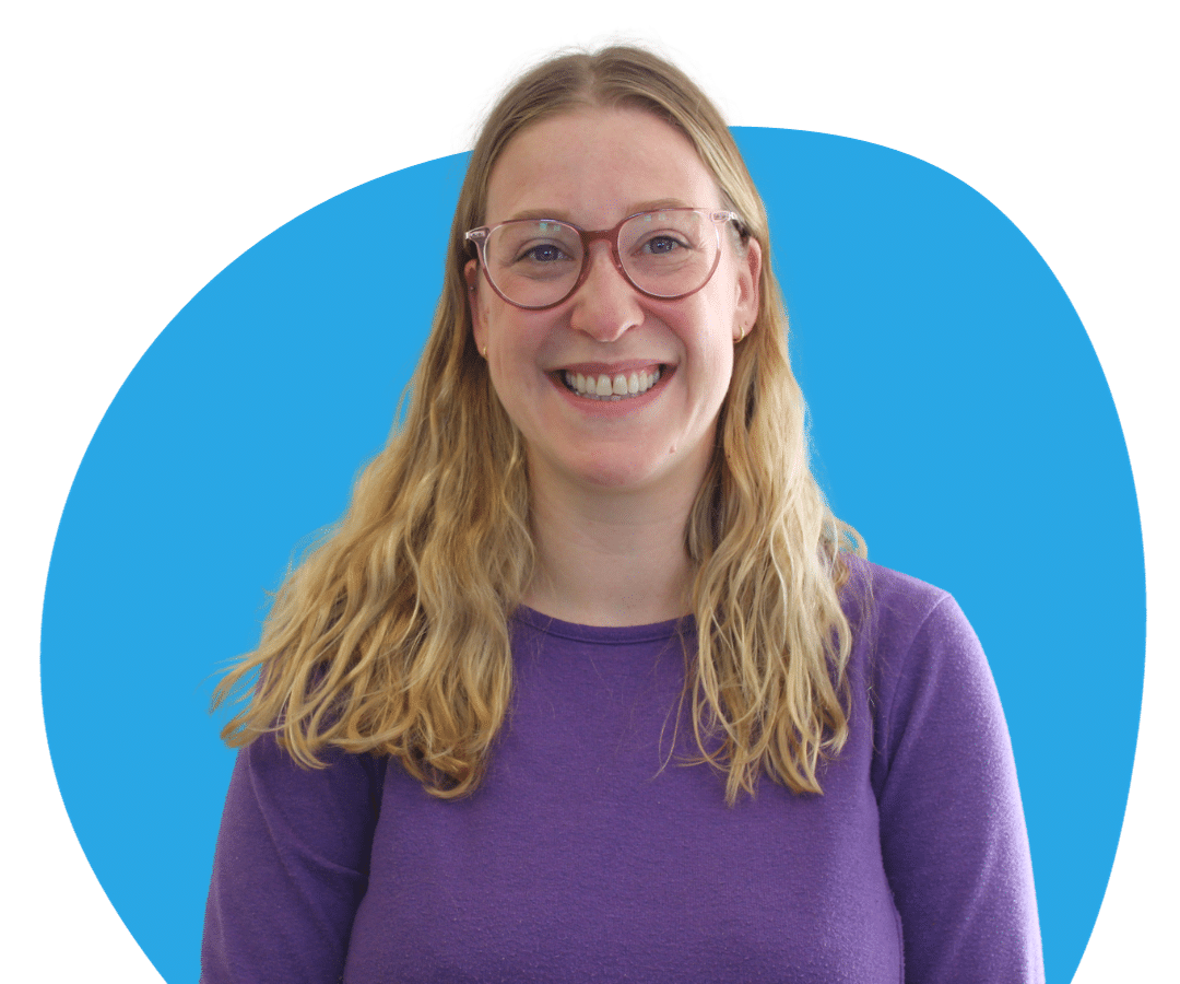 White woman with long, blonde, wavy hair and glasses against a light blue background.