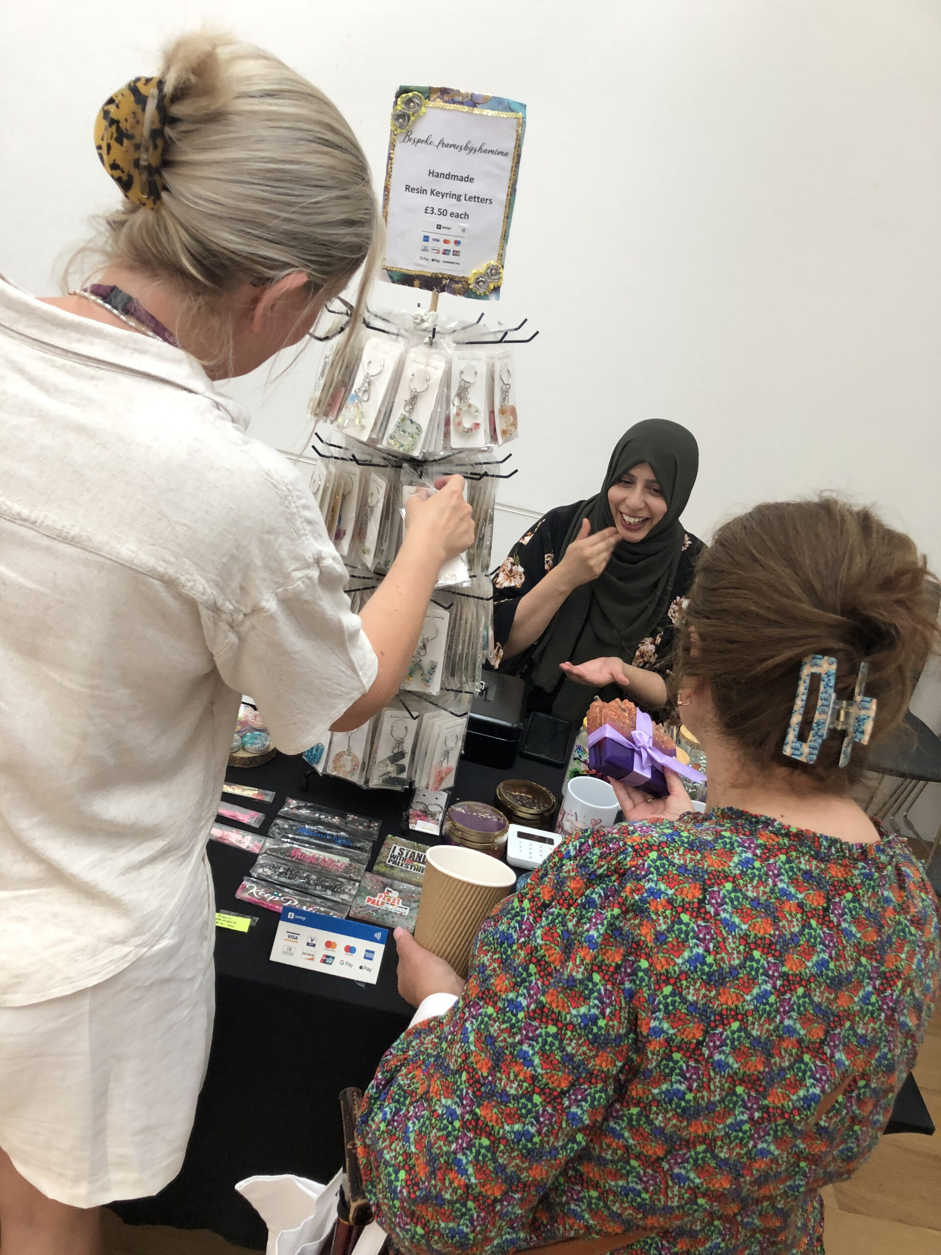 A woman is having a chat with a customer at her handmade gifts stall. Another potential customer is looking through keychains.