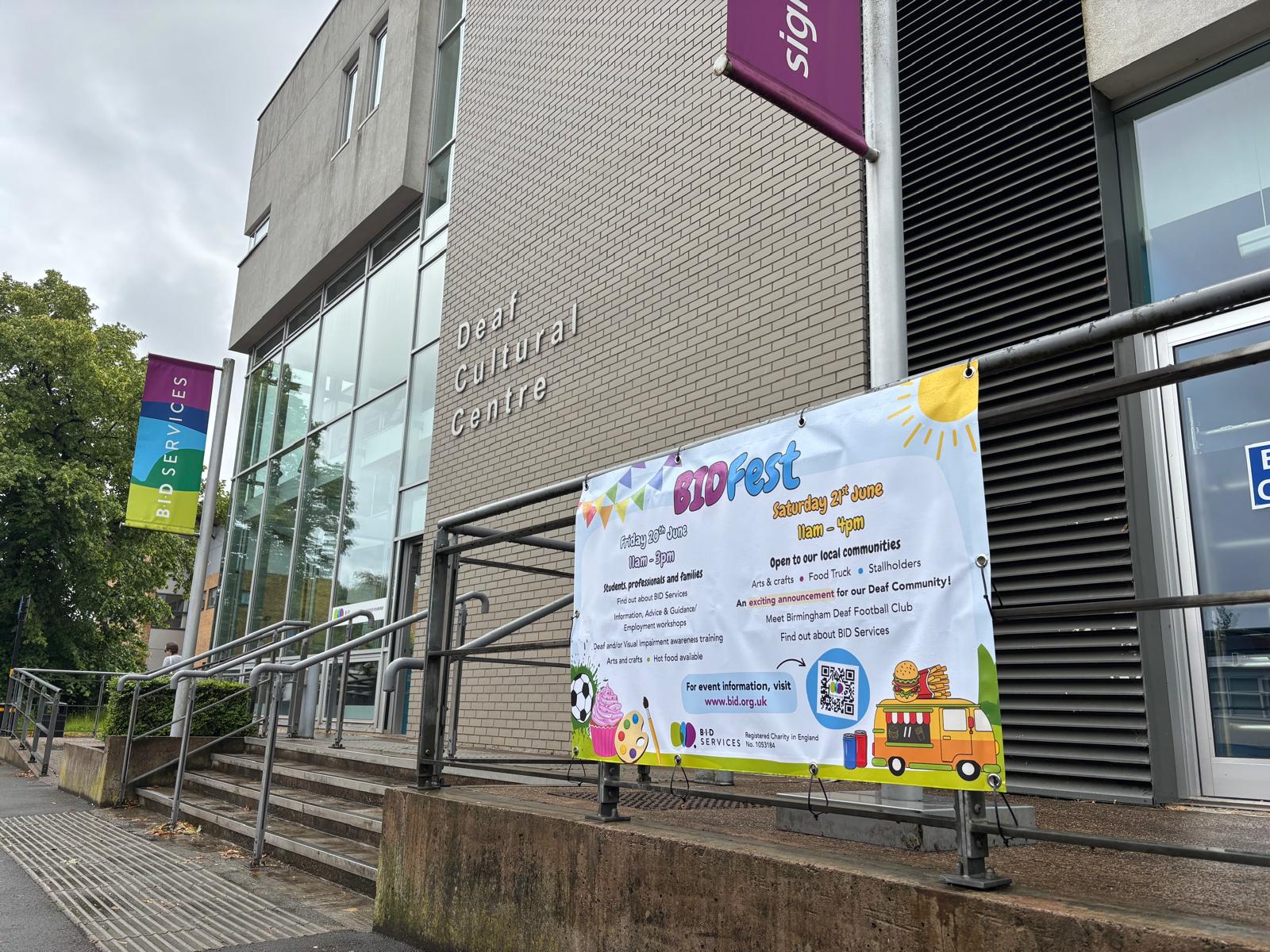 Deaf Cultural Centre building which is 2 stories tall, with light grey bricks and large windows. Focus in on the BID Fest decorative banner.