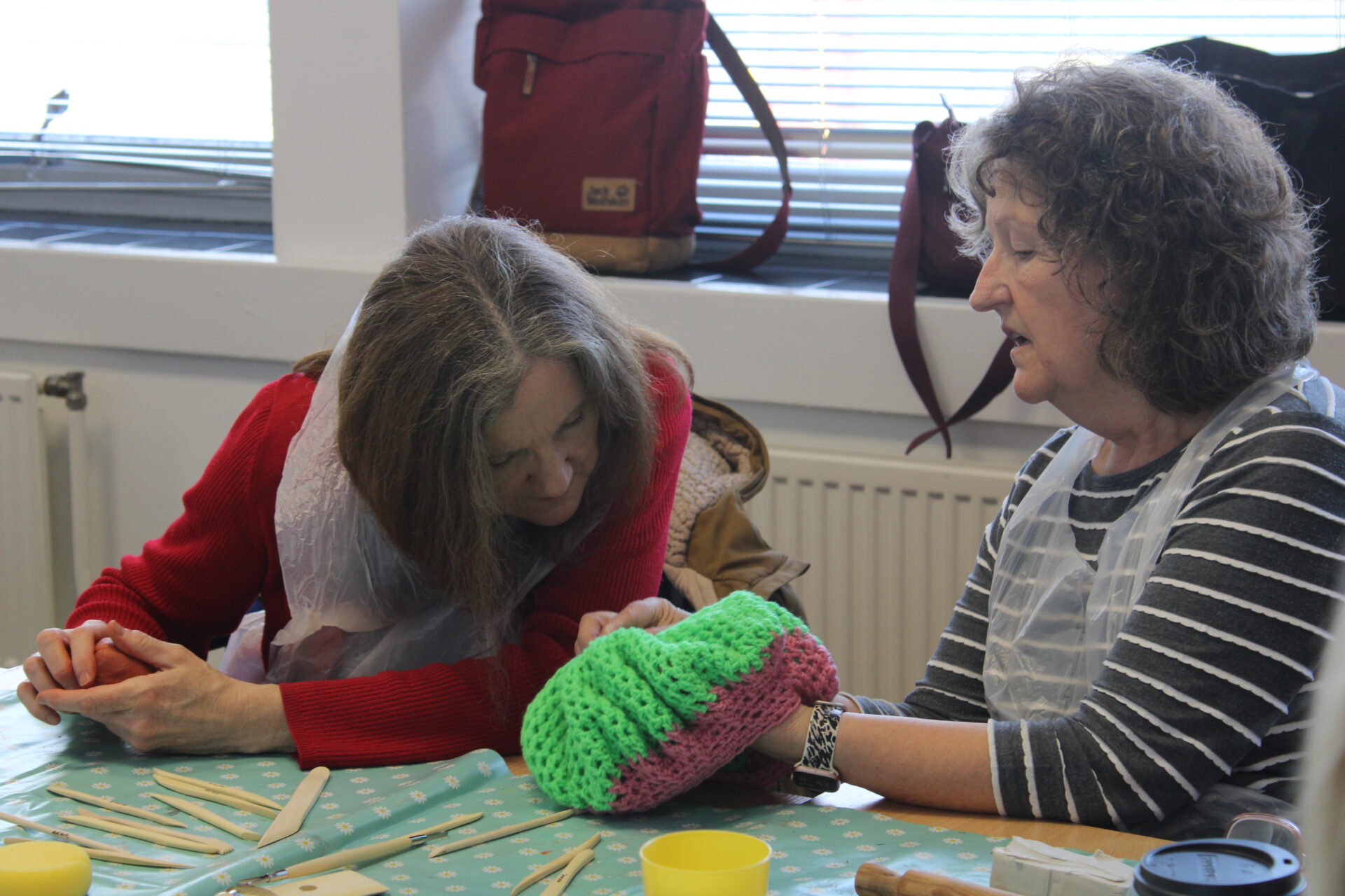 Two women are looking closely at a green and pink crotchet hat. 