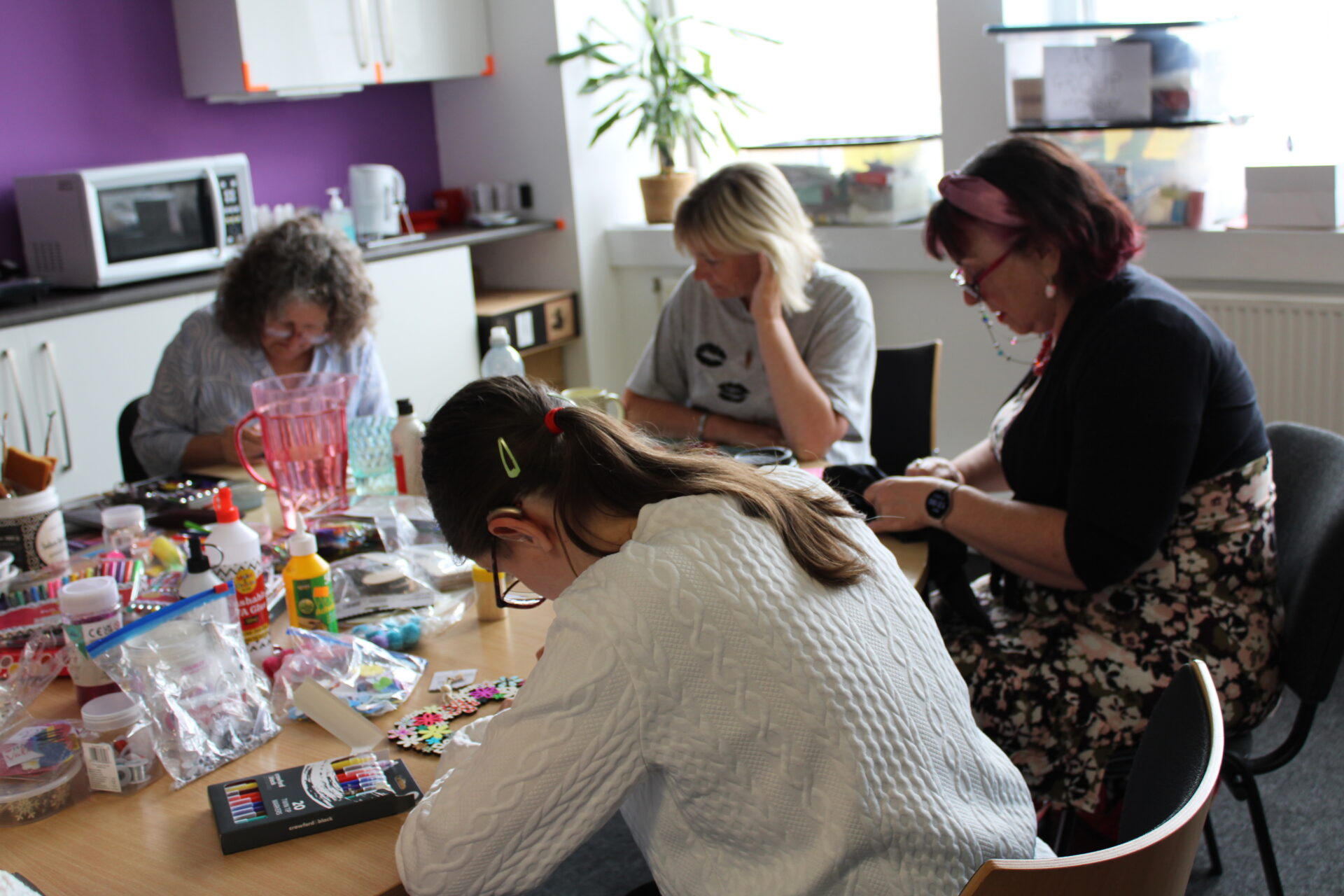 4 women sat around a table full of arts & crafts equipment. They look very focused on their tasks. 