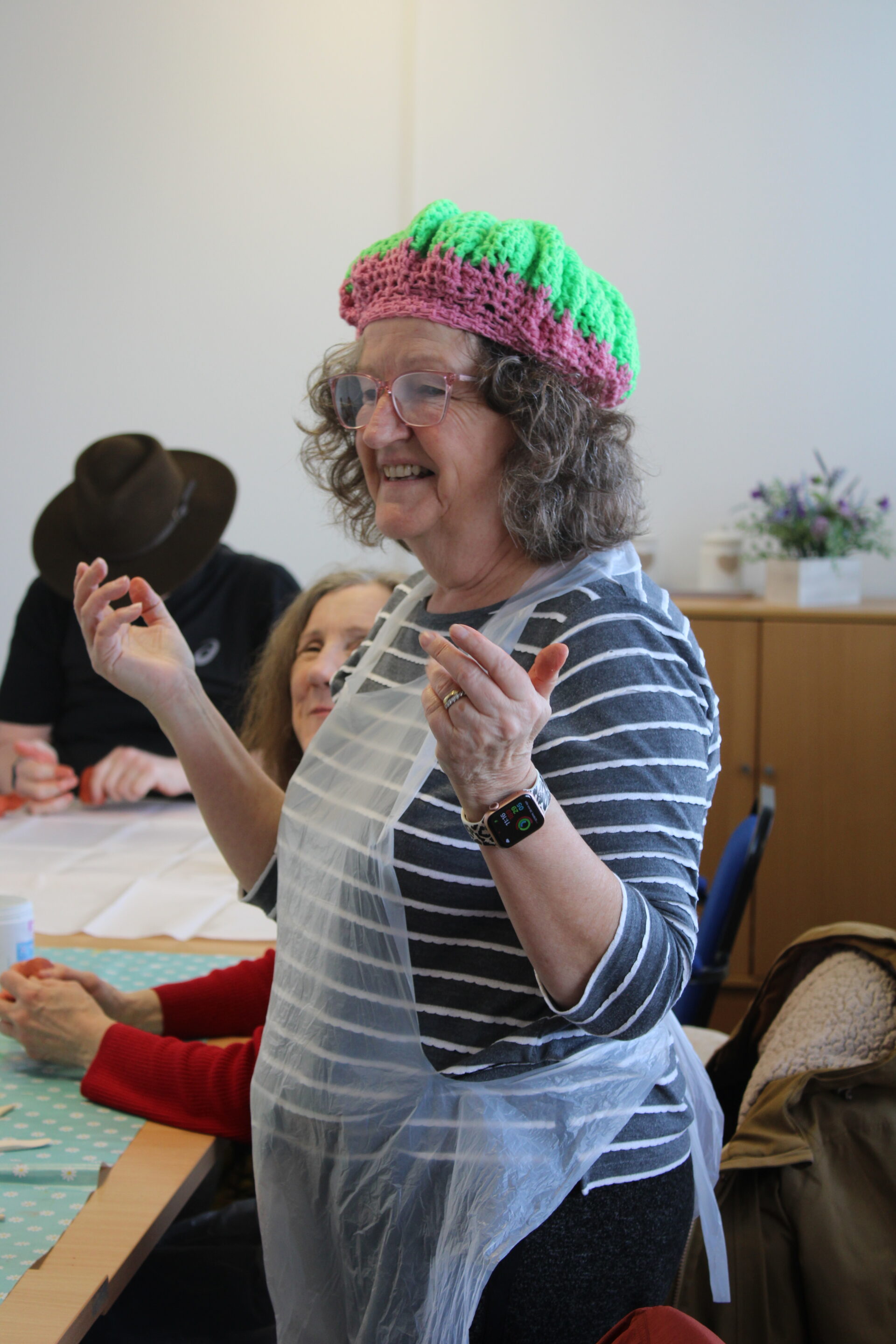 Volunteer, Angie is stood up and wearing her crocheted pink and lime green beret. 
